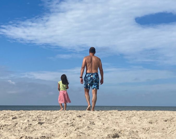 Silhouet van een vader en zijn dochter die samen de zee in lopen, genietend van quality time in de natuur.